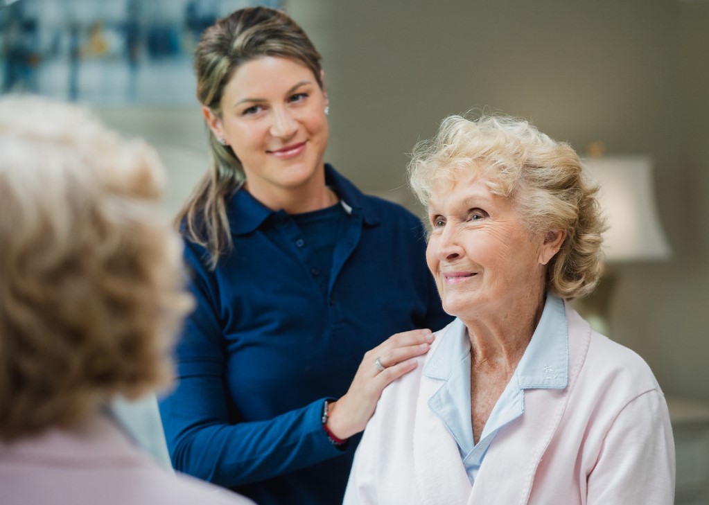 Staff member standing beside senior woman with hand on her shoulder